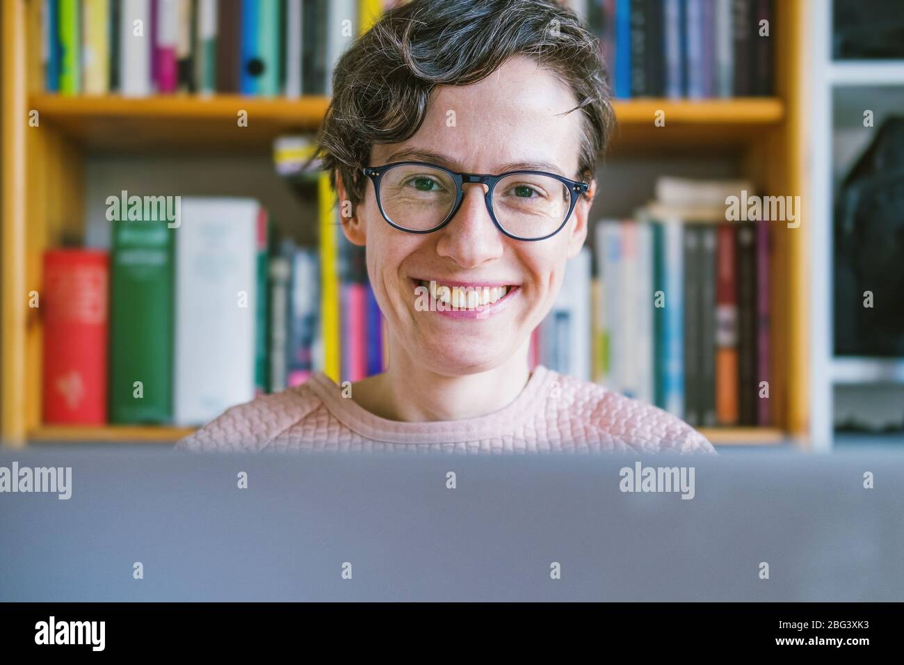 Woman working from home office. Young Caucasian short hair entrepreneur woman in sweater and glasses sitting and working online from home on computer Stock Photo
