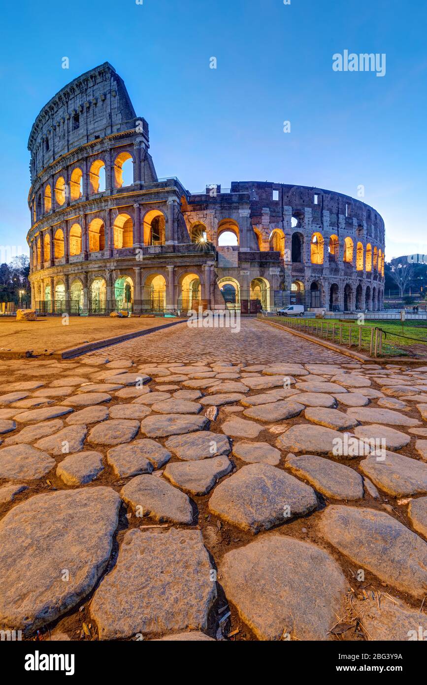 The illuminated Colosseum in Rome at dawn with big cobblestones in the foreground Stock Photo