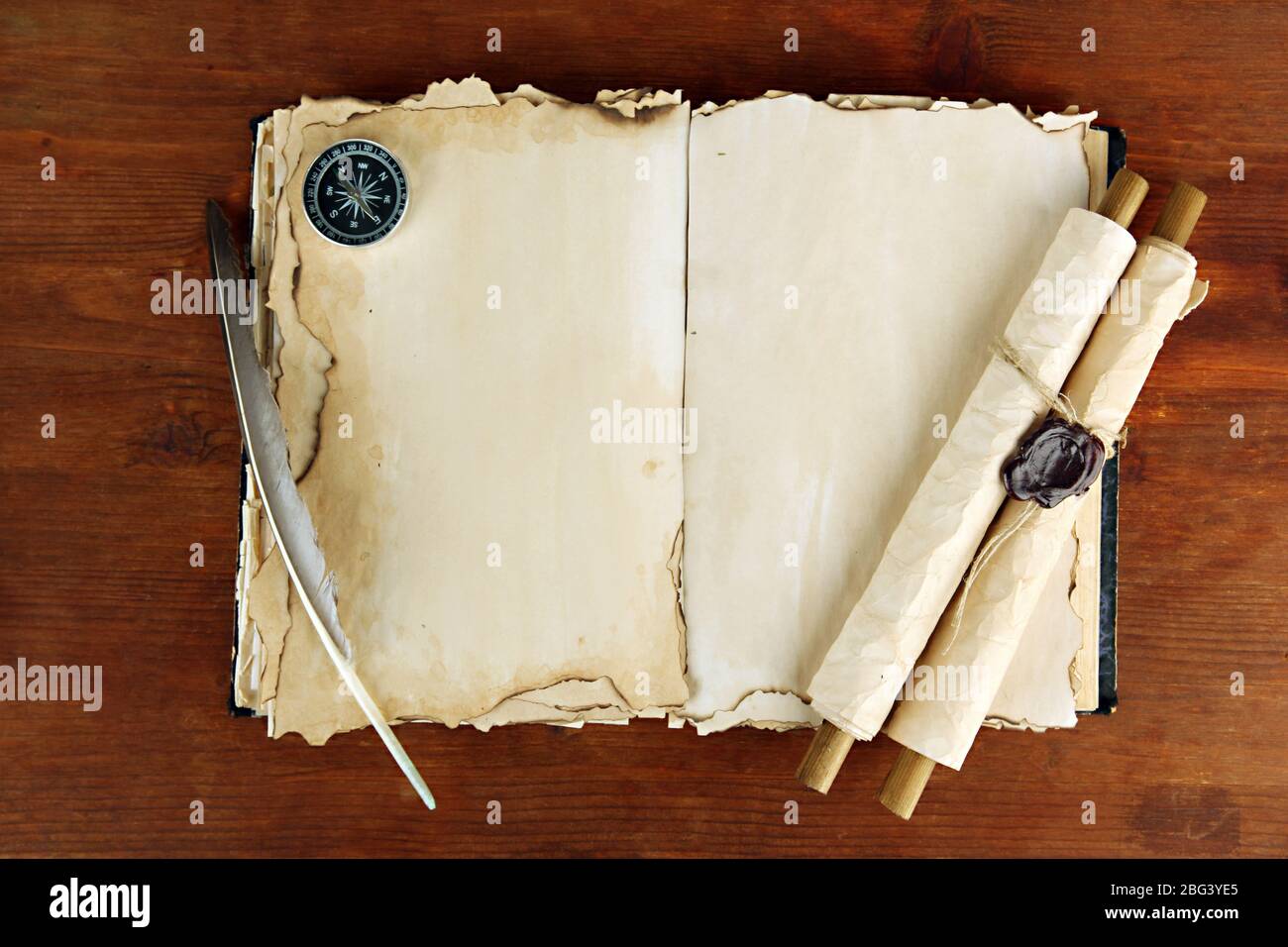 Open old book, scrolls and compass on wooden background Stock Photo