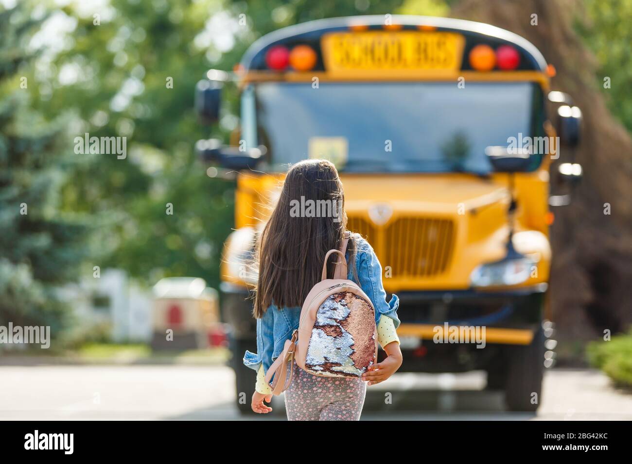 Little girl standing by a big school bus door with her pink backpack