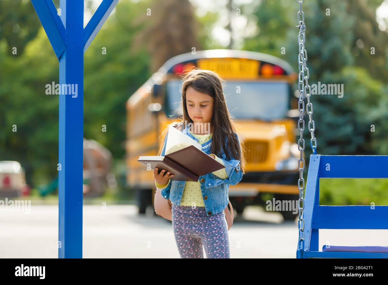 Little girl by a big school bus door with her pink backpack Stock Photo