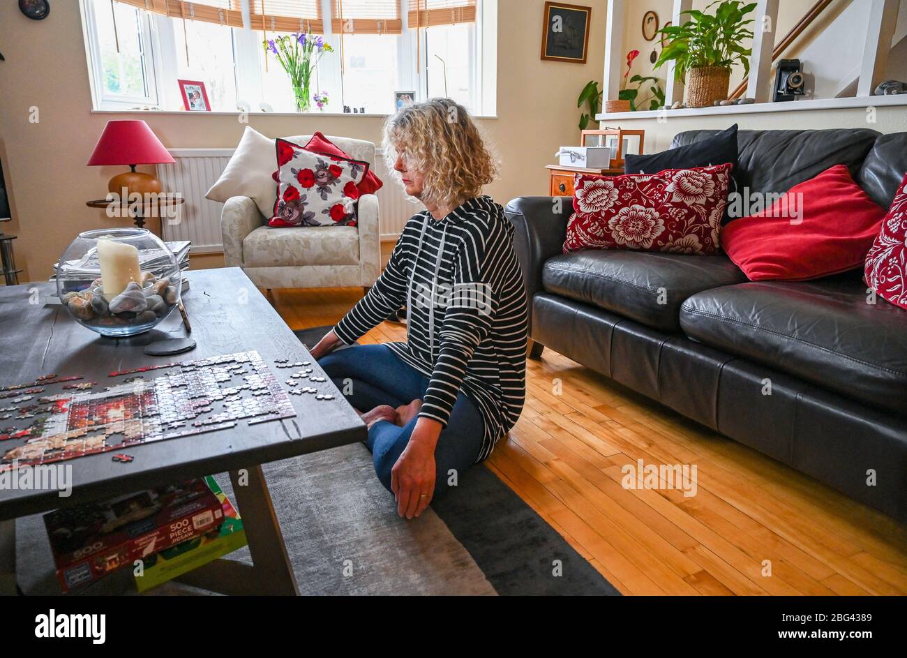 A mature middle aged woman doing relaxation mindfulness and breathing exercises at home watching a lesson on her smartphone Stock Photo