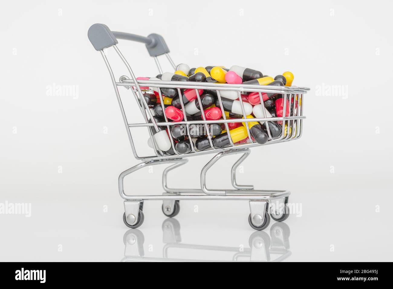 Mini shopping trolley full of colourful pills caplets. Metaphor Big