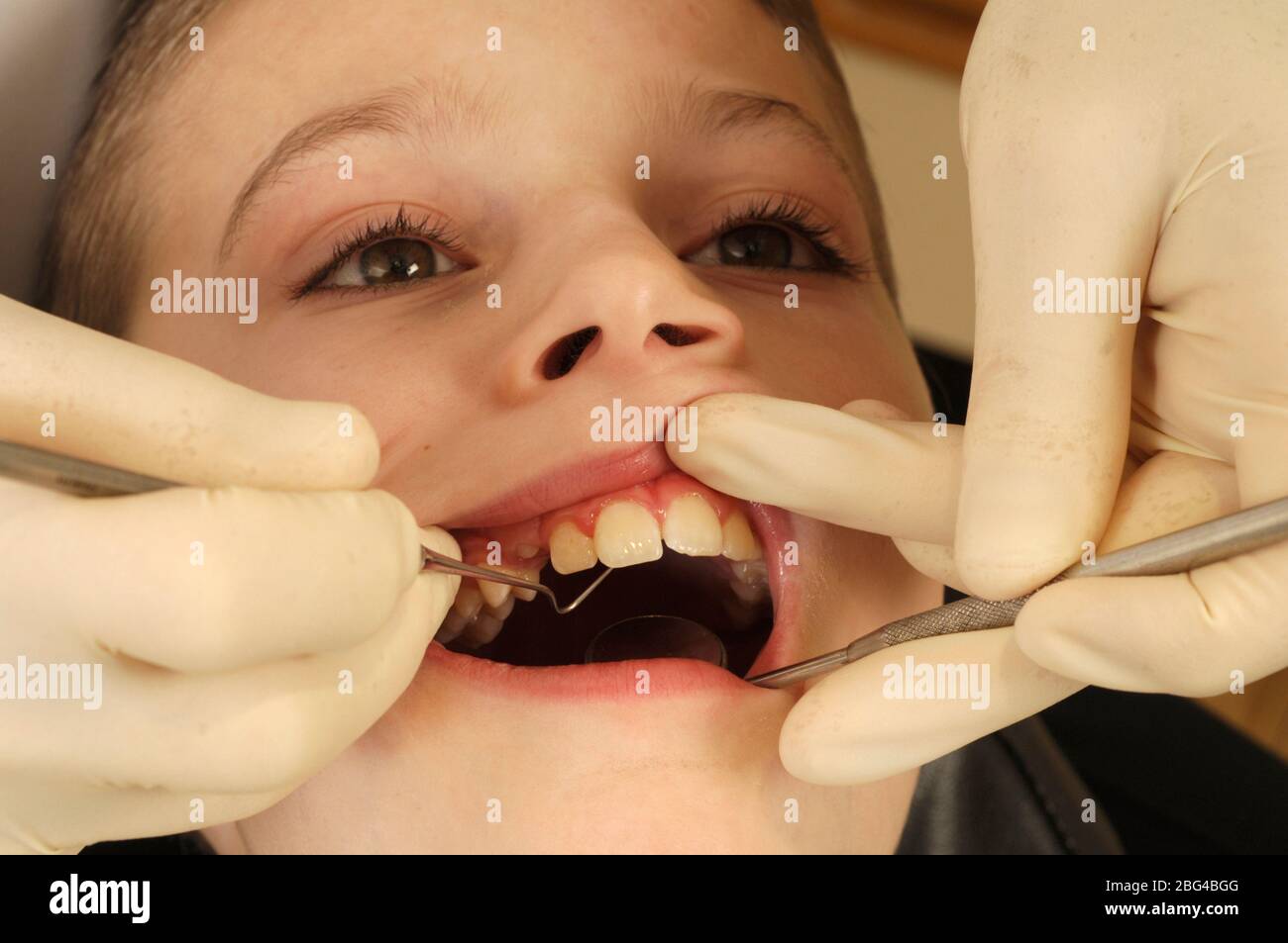 A young boy has his teeth examined by a dentist who uses a dental pick
