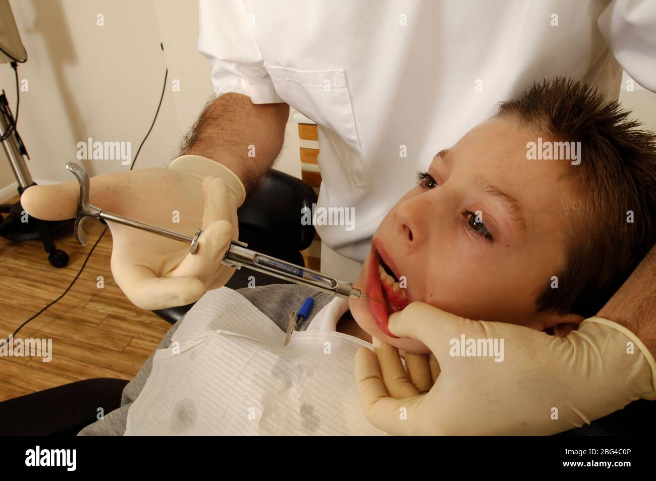 A dentist injecting an anaesthetic into a young boy's gums to cause