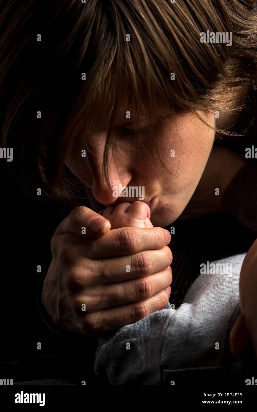 Close up Shot of Loving Mother Kissing the Small Hand of her Sleeping Baby on Black Background. Stock Photo