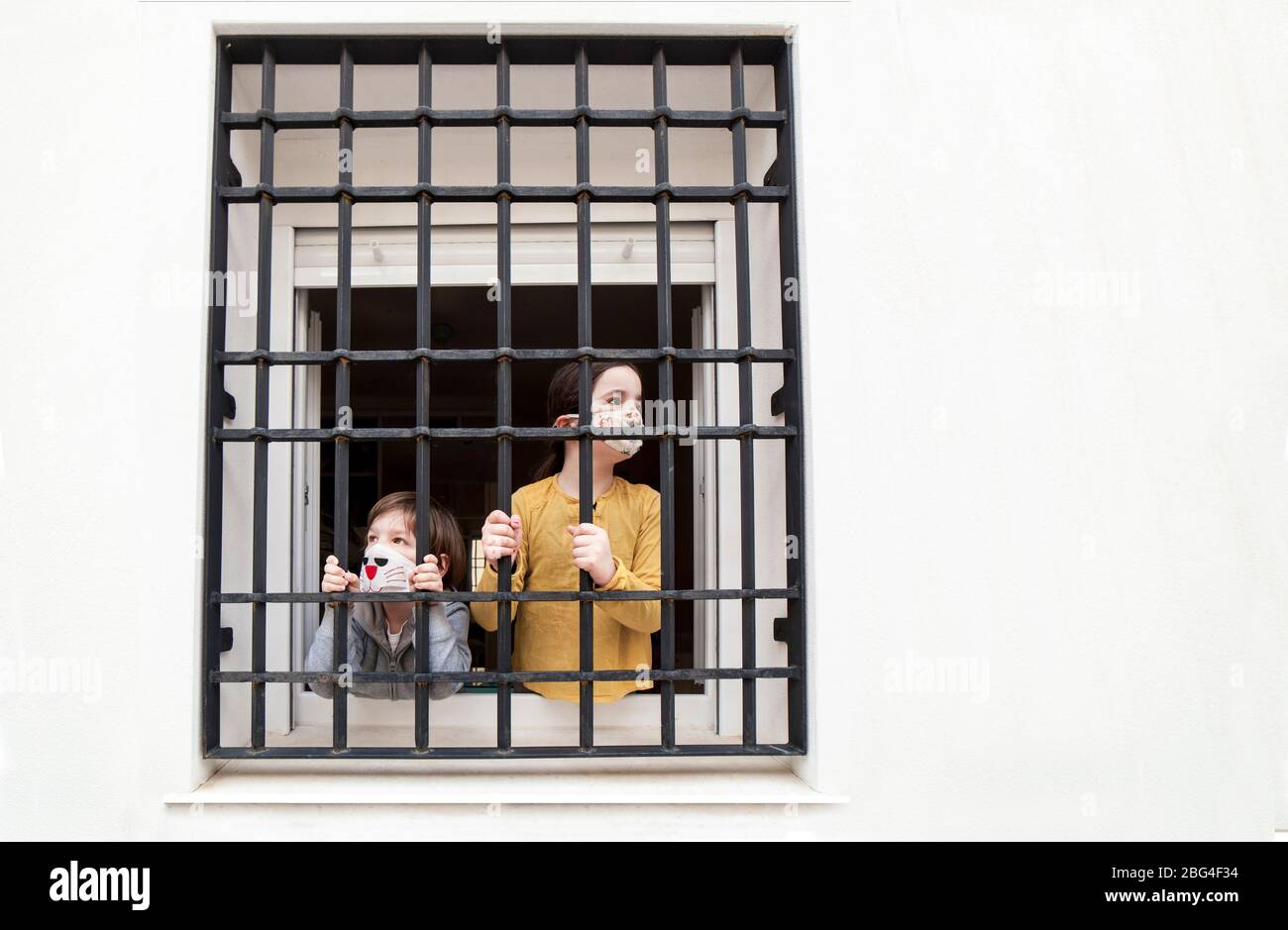 Two children look sadly outdoors through wrought-iron window. Impact on children of Covid-19 confinement Stock Photo