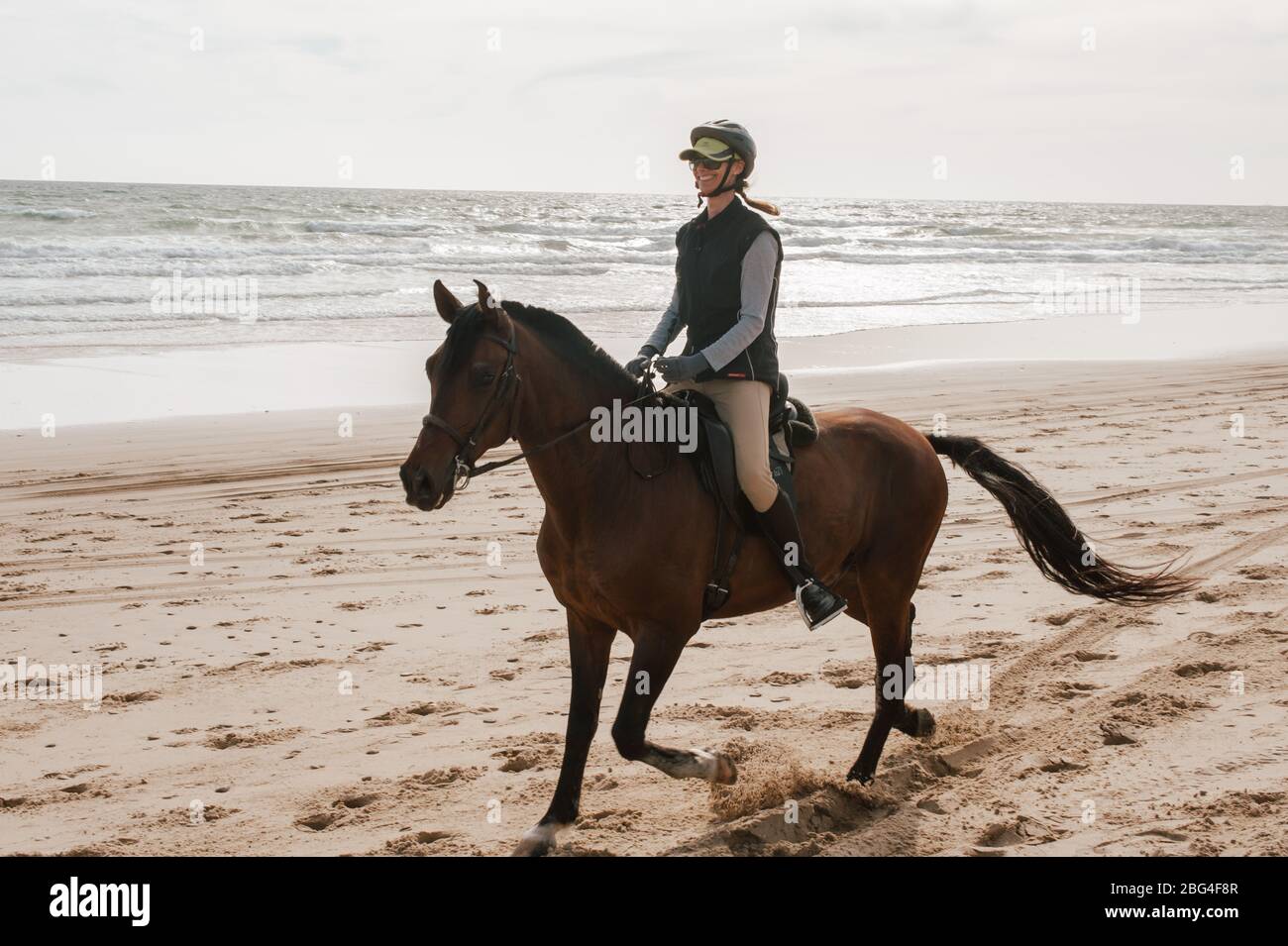 Woman riding Andalusian horse on the beach and smiling Stock Photo