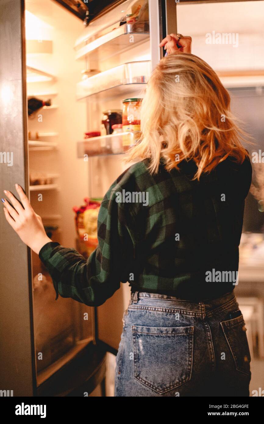 Young hungry woman looking in open refrigerator at home Stock Photo