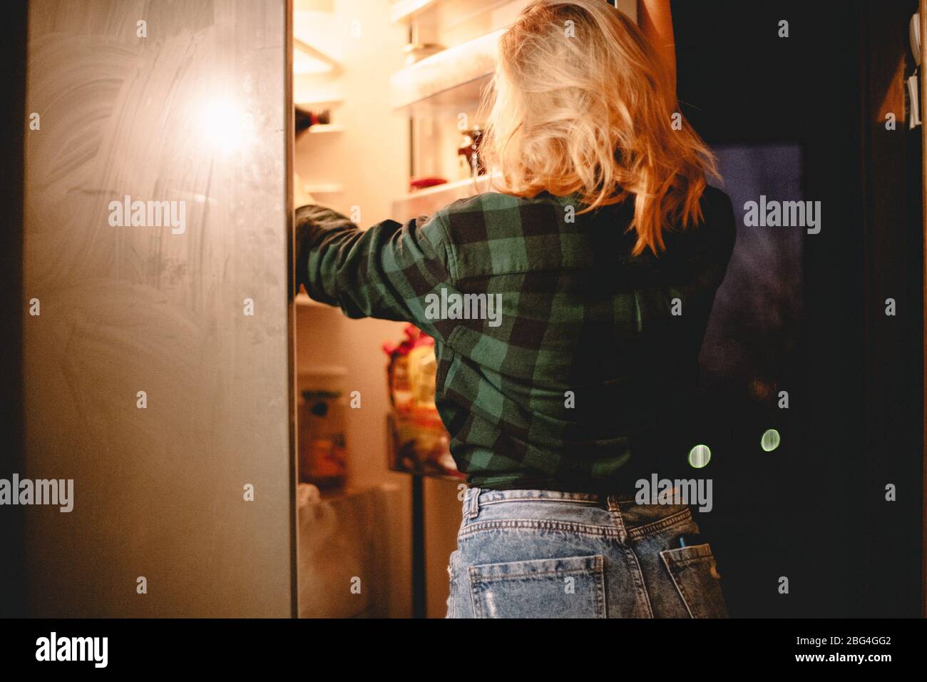 Young hungry woman looking for food in fridge at night at home Stock Photo