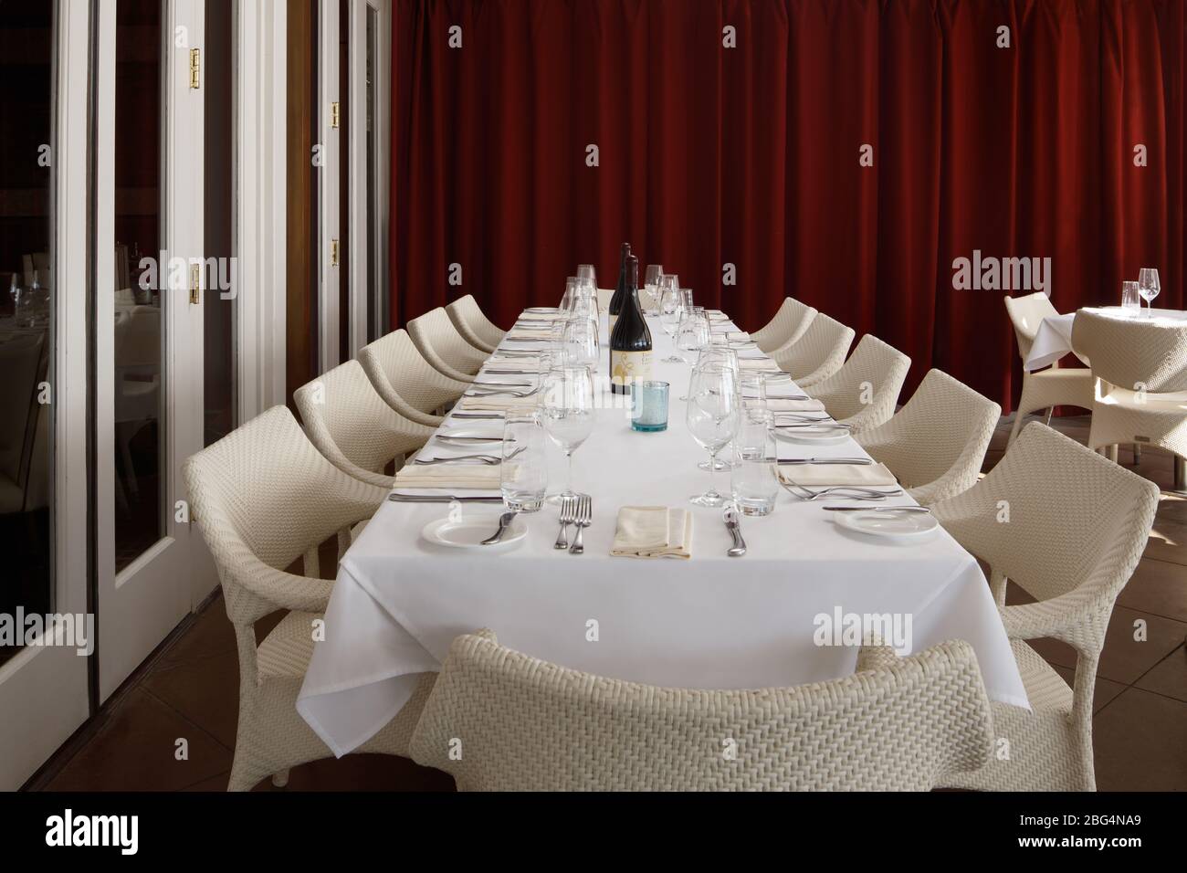 A white table with white linen and white chairs next to red wall Stock Photo