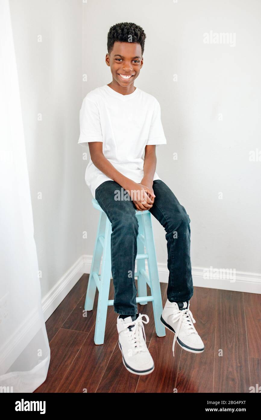 Happy preteen black boy in tshirt, jeans & sneakers on blue stool Stock Photo