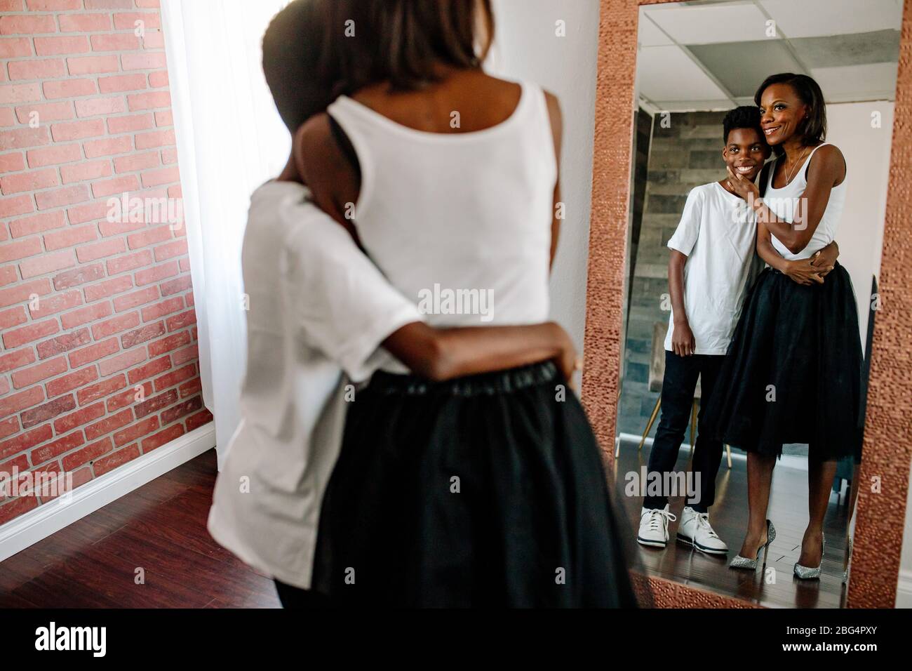 Mirror view of black boy hugging pretty mom wearing white shirts Stock Photo