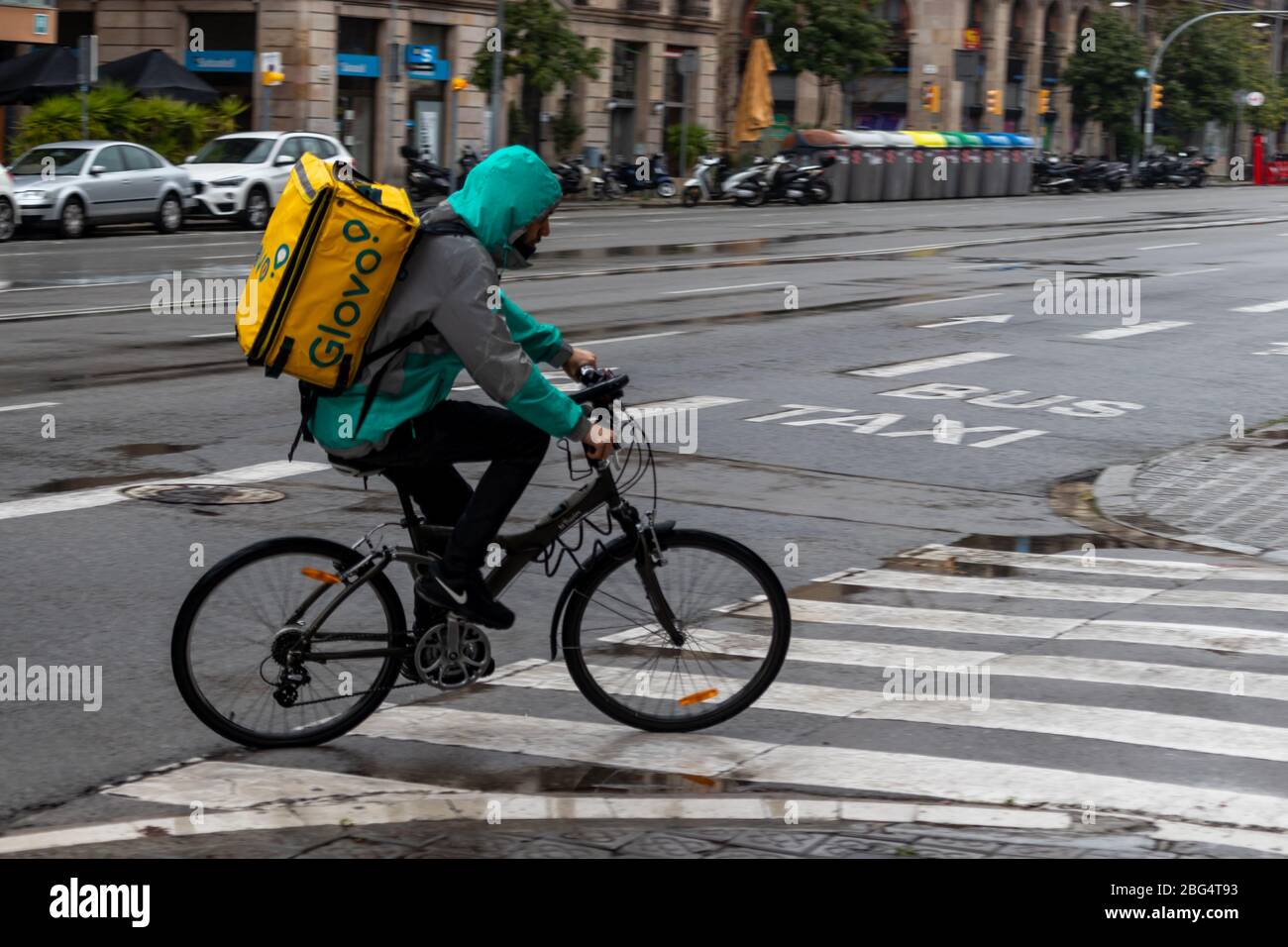 Barcelona, Spain. 20th Apr, 2020. Glovo deliveryman cycling through the empty streets of Barcelona under the rain Stock Photo