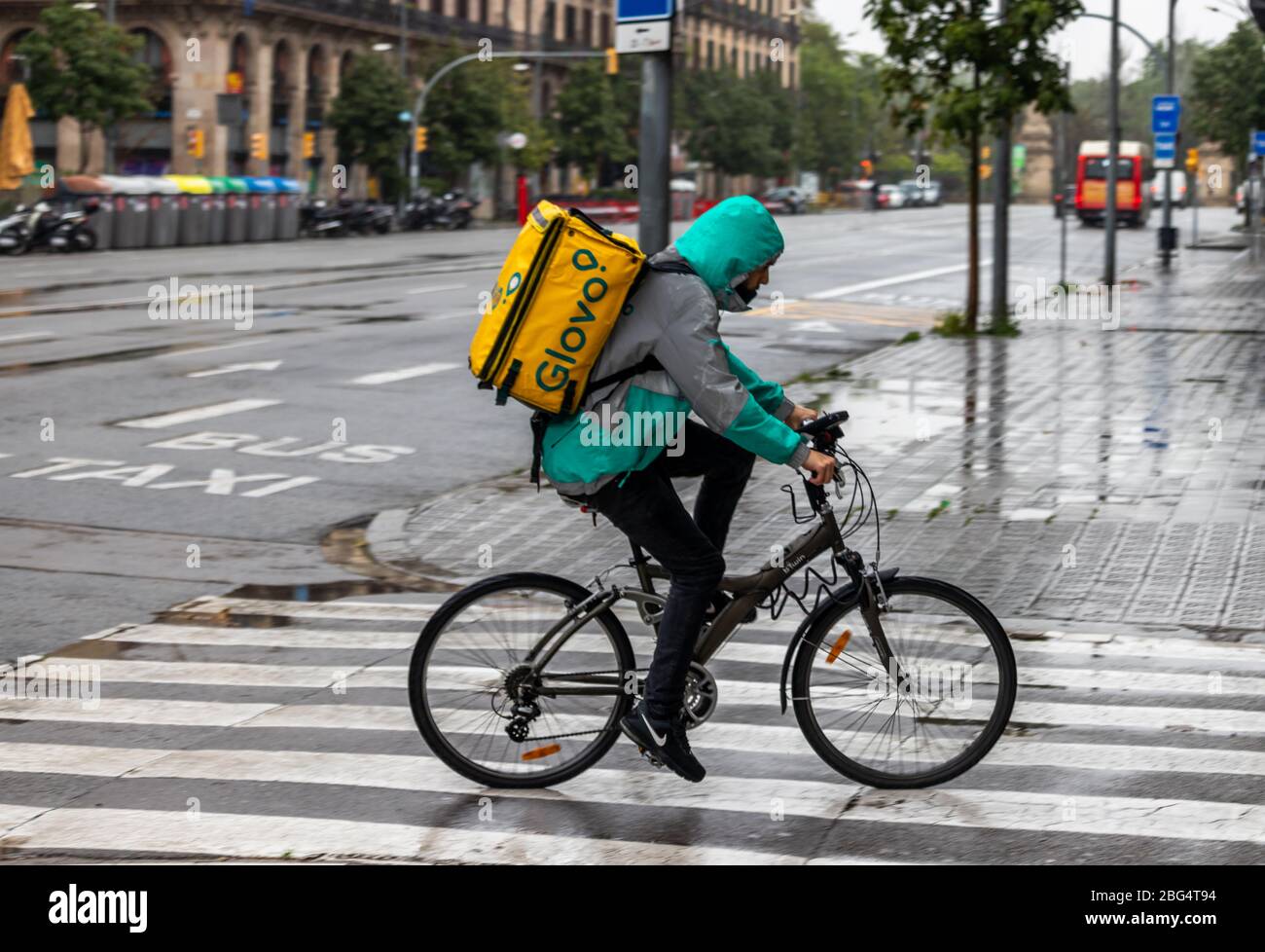 Barcelona, Spain. 20th Apr, 2020. Glovo deliveryman cycling through the empty streets of Barcelona under the rain Stock Photo