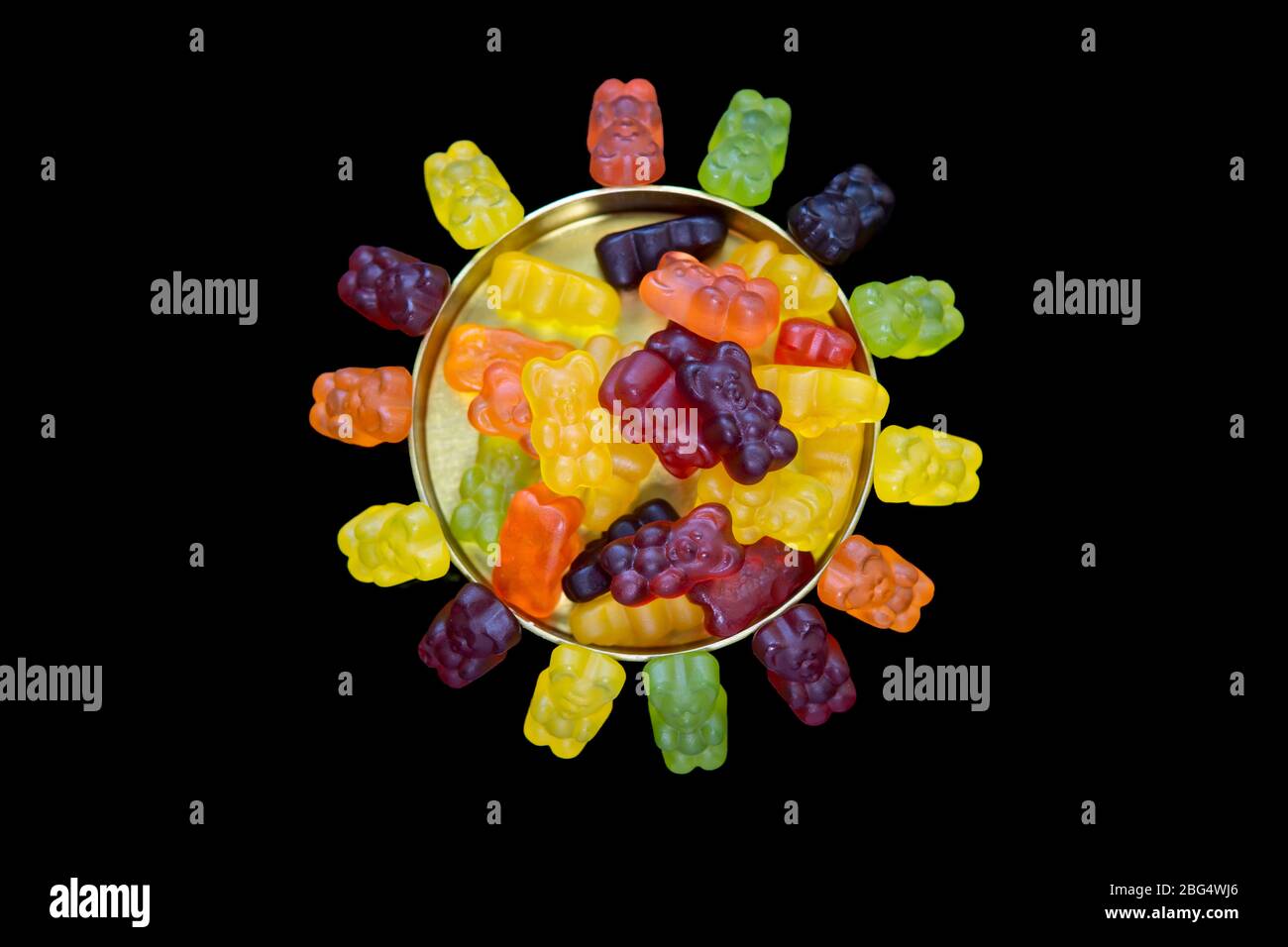 Gummy bears in a metal candy box and around it forming the sun on a black background Stock Photo