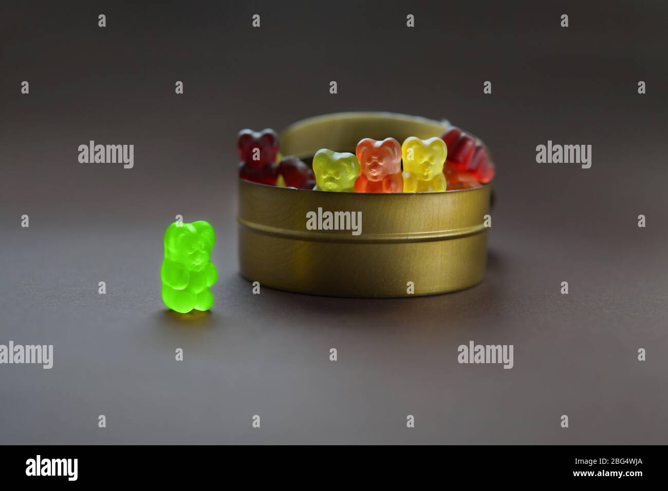 One gummy bear stands apart from a group of other jelly bears sharing the same candy jar. Discrimination concept: being an outcast and outsider. Stock Photo