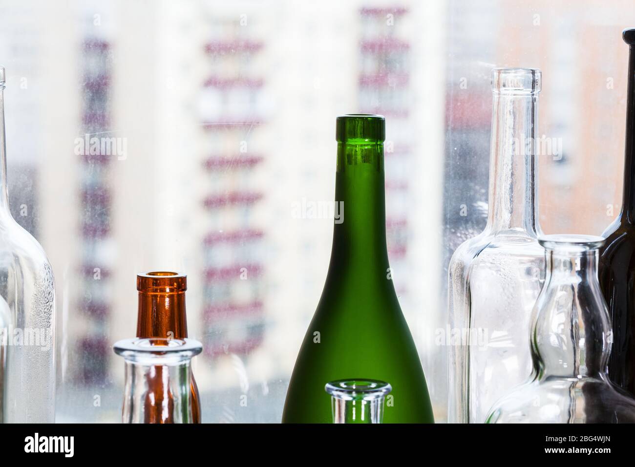 several empty bottles and view of urban houses through home window on background Stock Photo