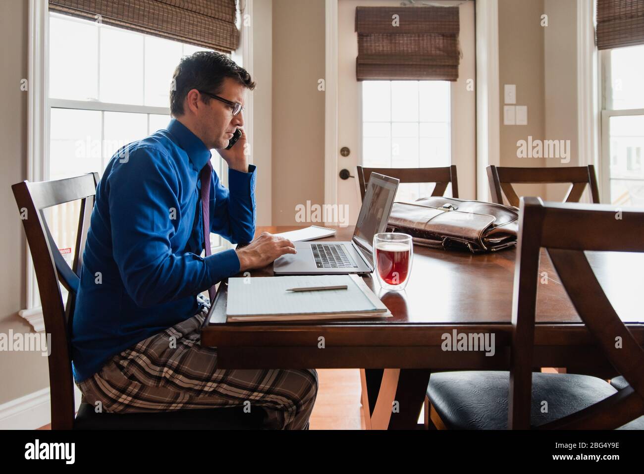 Man on cellphone working from home using a computer in pyjama pants. Stock Photo