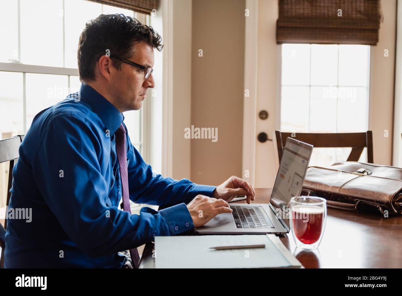 Man in shirt and tie working from home using computer at dining table. Stock Photo