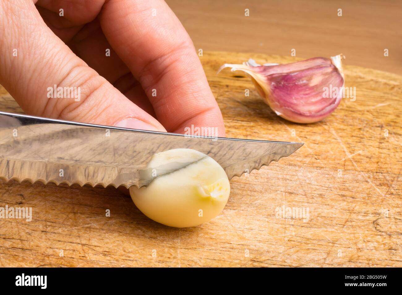 hand slicing garlic cloves on the cutting board with a knife Stock Photo