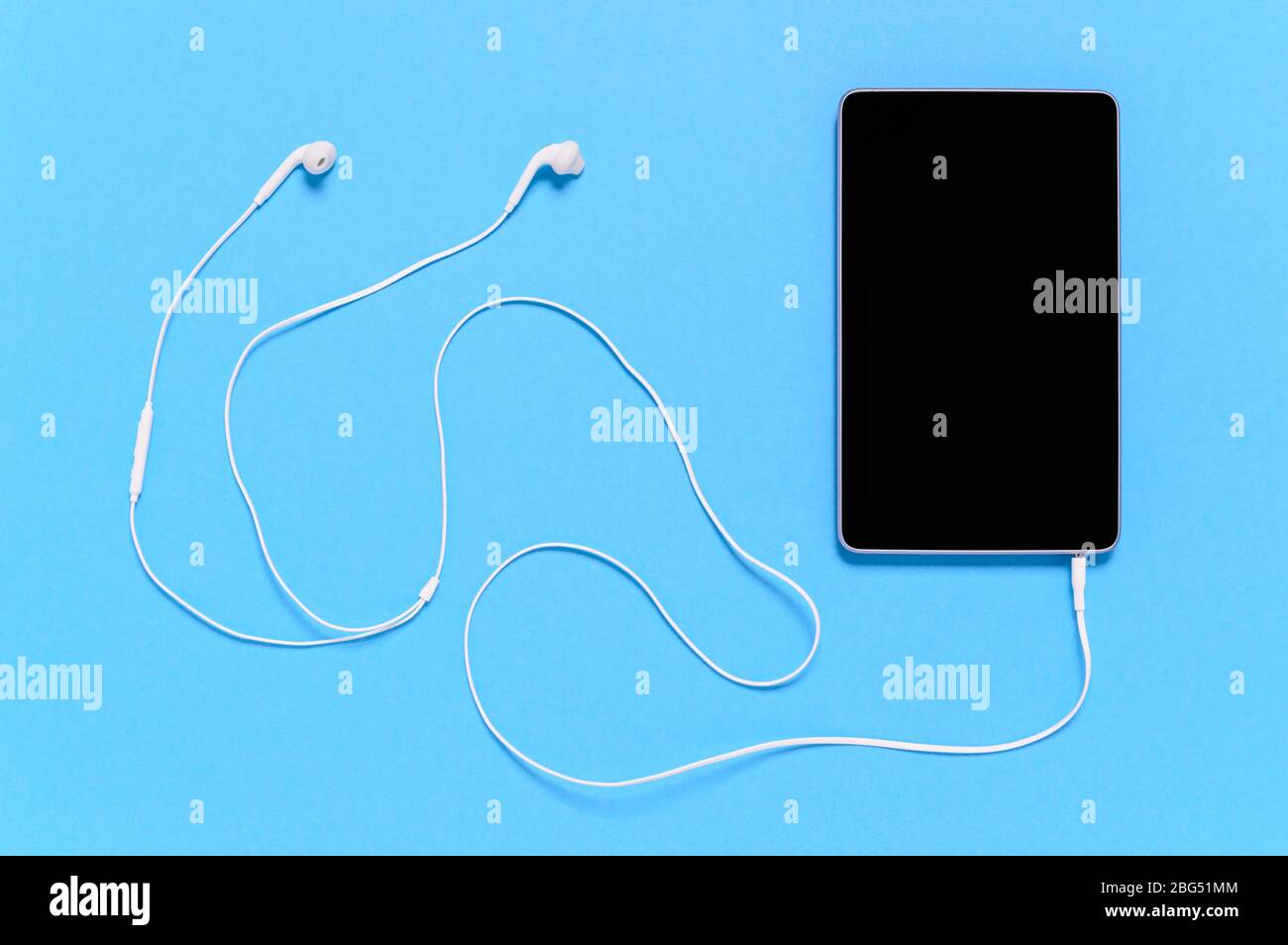 Black tablet with white earphones on blue background. Minimal concept of connectivity, remote digital work or multimedia entertainment like music stre Stock Photo