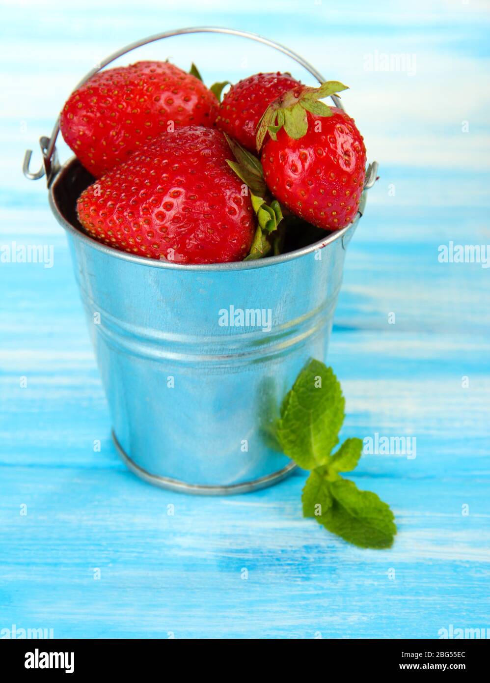 Ripe sweet strawberries in metal pail on blue wooden table Stock Photo ...