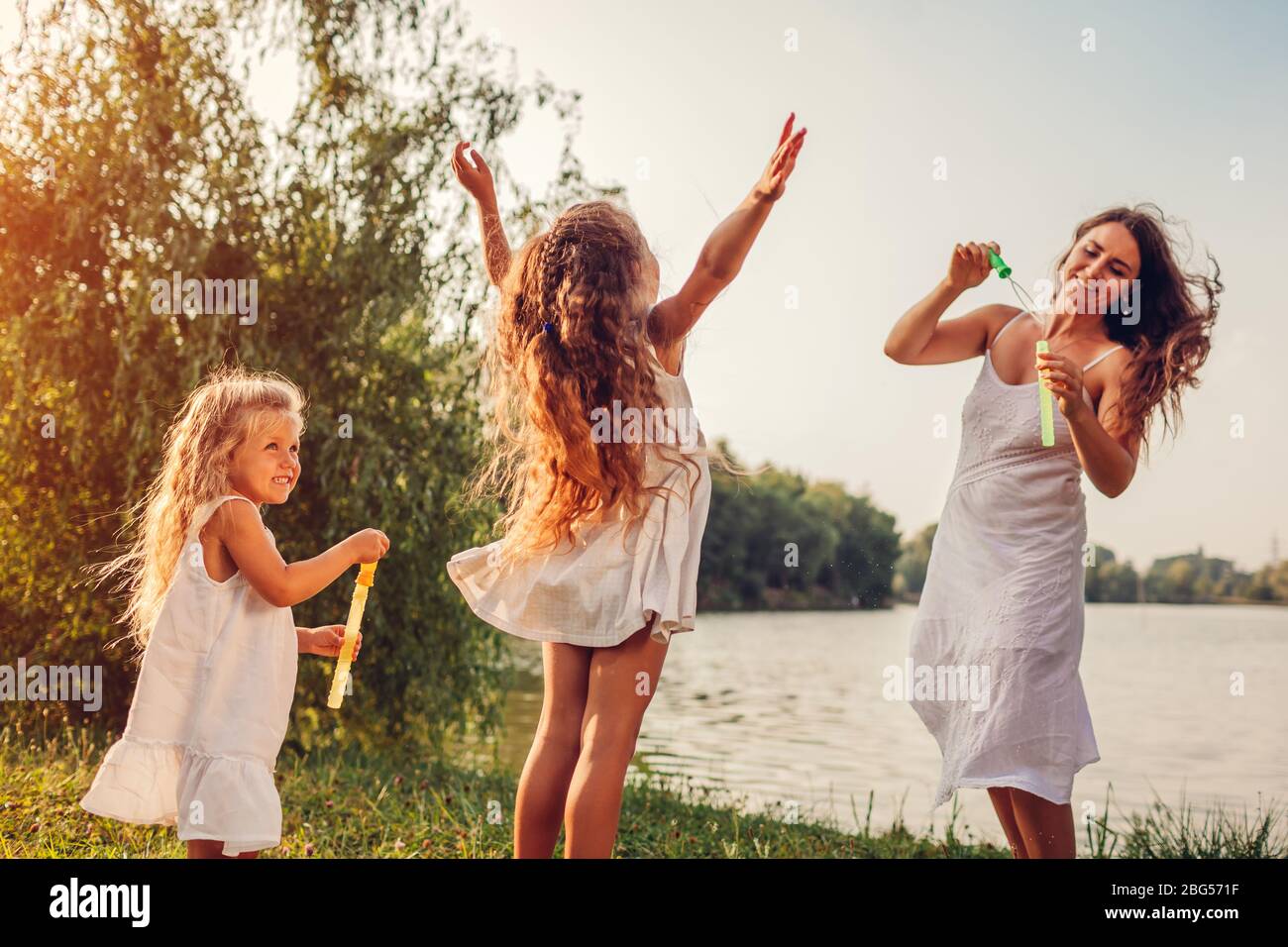 Mother's day. Mother helps daughters to blow bubbles in spring park
