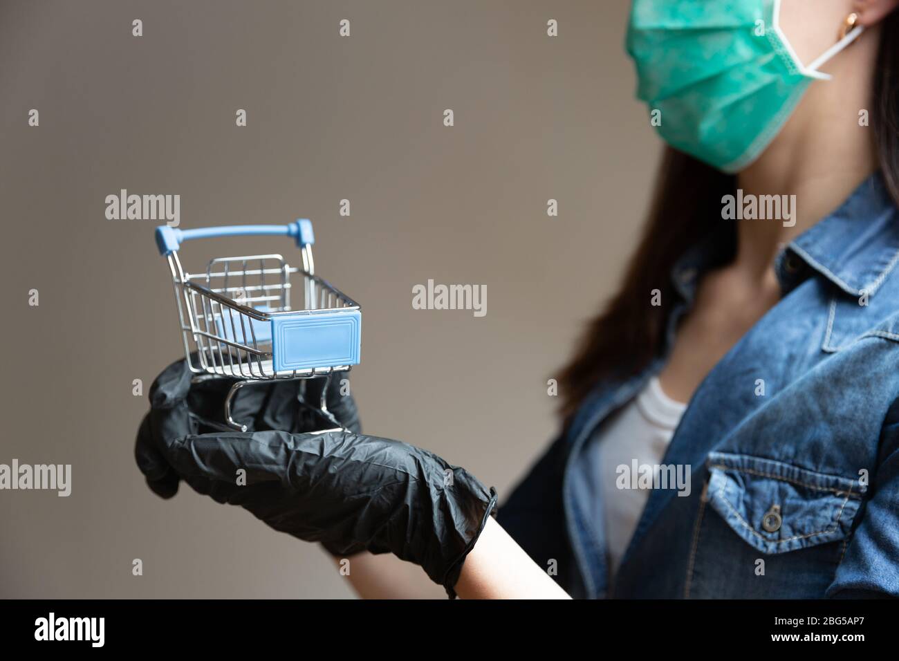 Woman wearing facial medical holding in hands with black gloves shopping cart. Shopping in pandemic concept Stock Photo