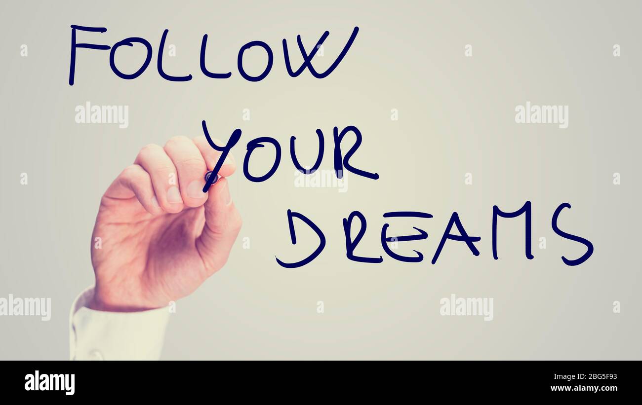Retro instagram style image of a male hand writing motivational message Follow your dreams on virtual board. Stock Photo