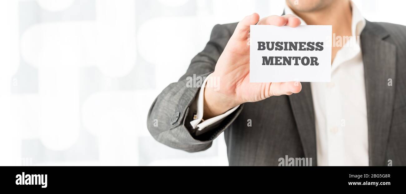 Businessman holding up a small white card with the words Business Mentor in a concept of consulting, advice, skill and experience. Stock Photo
