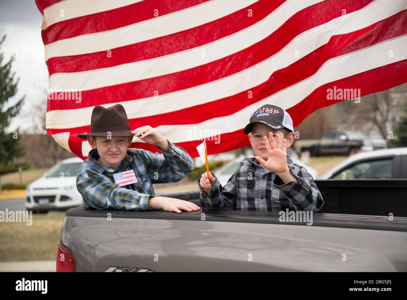 Helena, Montana - April 19, 2020: Boys riding in the back of a truck at a protest holding paper American flags and wearing a Trump 2020 hat. Children Stock Photo