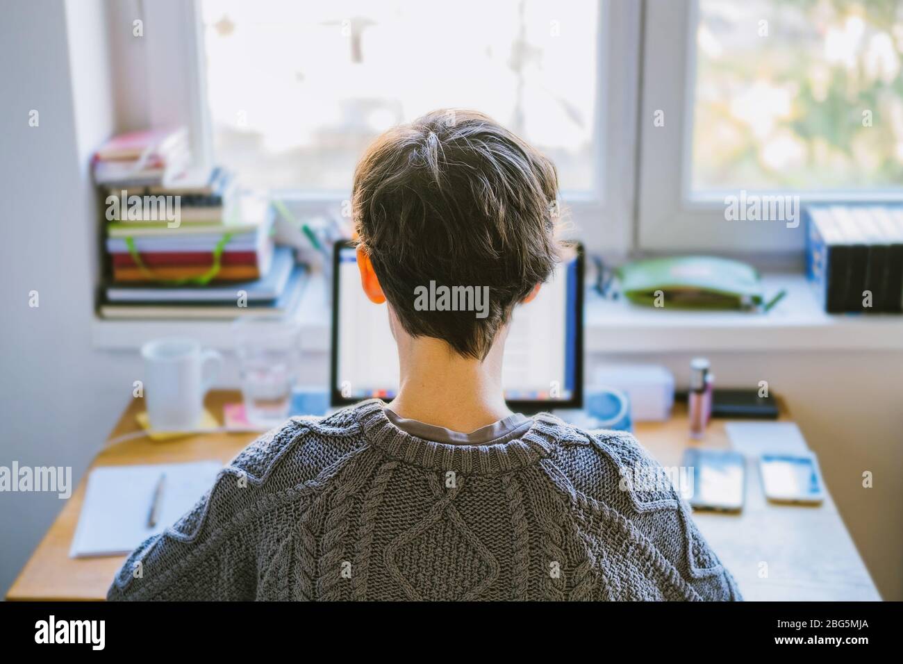 Woman working from home office. Young Caucasian short hair entrepreneur woman in sweater and glasses sitting and working online from home on computer Stock Photo