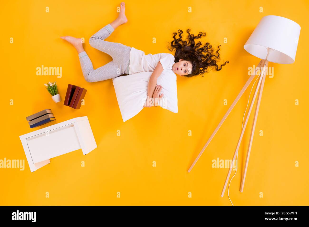 Full body high angle above flatlay photo of beautiful little lady lying hug pillow comfy floor near book shelf lamp open mouth wear pajama isolated Stock Photo