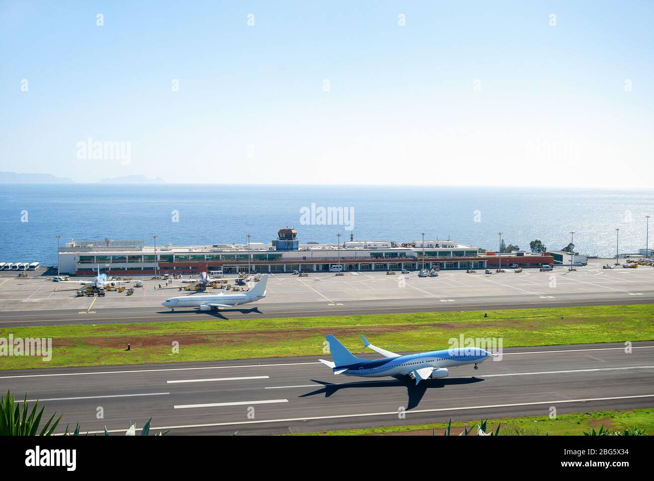 Aerial view of airplane taking off runway at Madeira international airport, airplanes by terminal building and seascape in background, Portugal Stock Photo