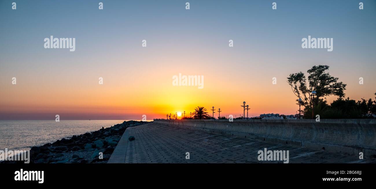 Sea embankment with orange-red sunset with silhouettes of lanterns. Sea embankment in the orange light of the setting sun. Bright sunset at Sea Embank Stock Photo