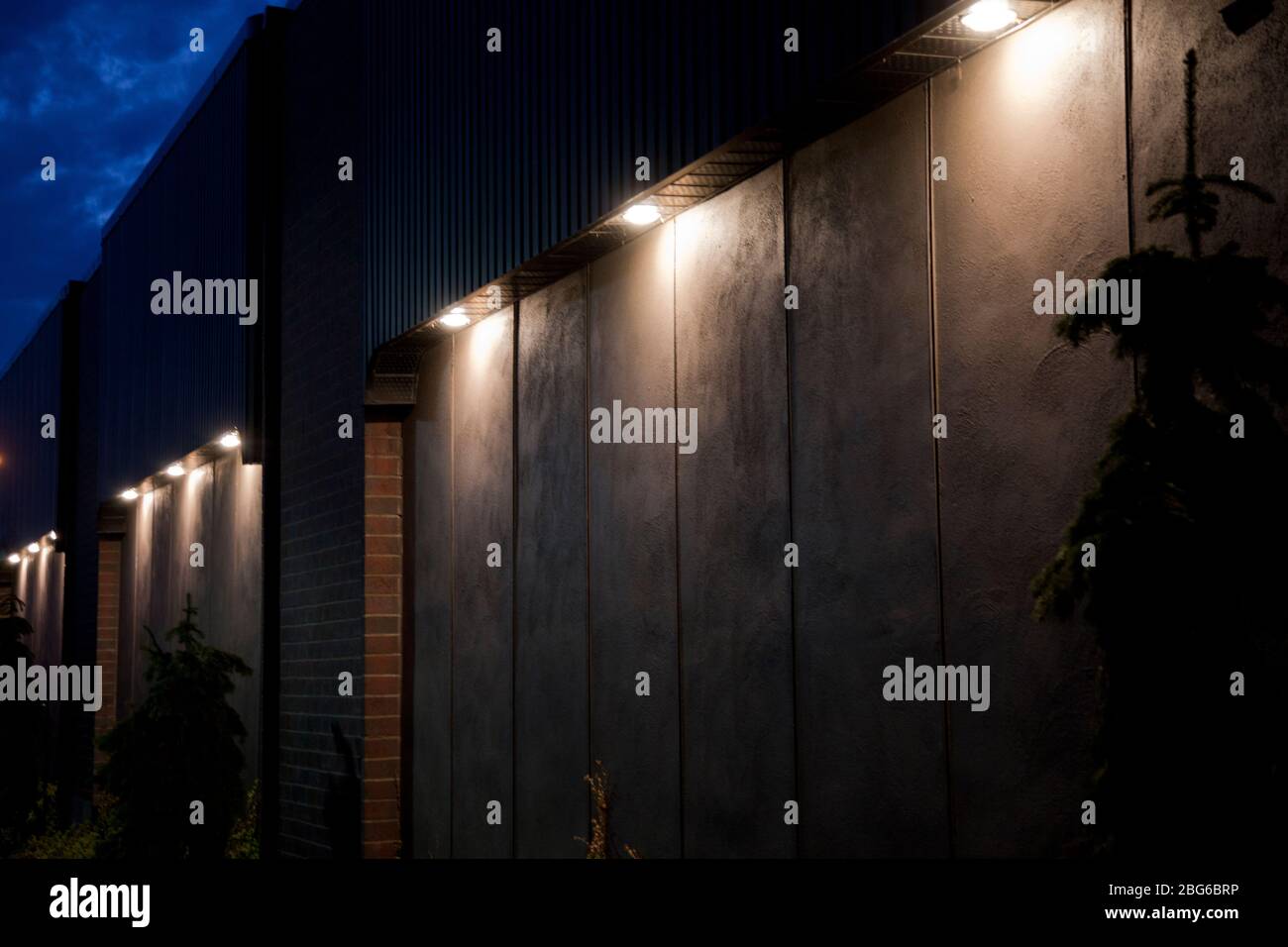 Large pot lights illuminating a concrete wall with bricks at twilight. Illuminated blank building wall in the dark. Stock Photo