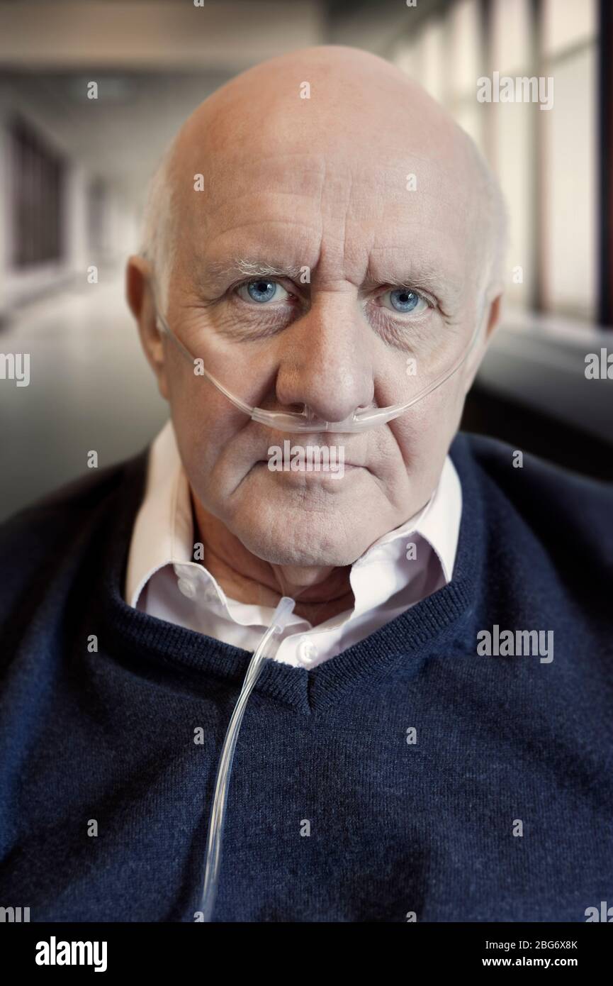 Portrait of an elderly / old / mature man wearing a cannula oxygen nasal tube. Hospital corridor in the background Stock Photo