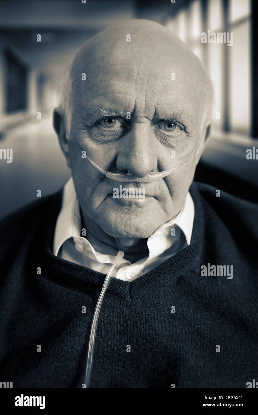 Portrait of an elderly / old / mature man wearing a cannula oxygen nasal tube. Hospital corridor in the background Stock Photo