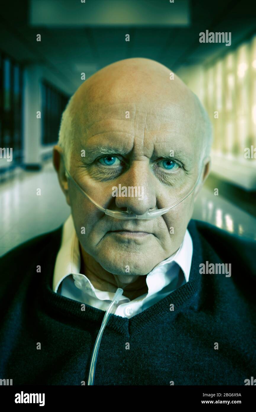 Portrait of an elderly / old / mature man wearing a cannula oxygen nasal tube. Hospital corridor in the background Stock Photo