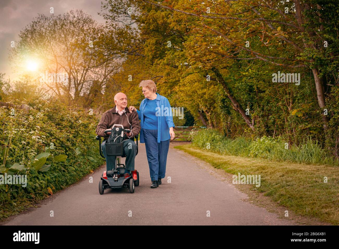 Mature Old Elderly happily married couple out in the countryside while one drives a motorised Mobility Scooter. Healthcare Carer concept Stock Photo