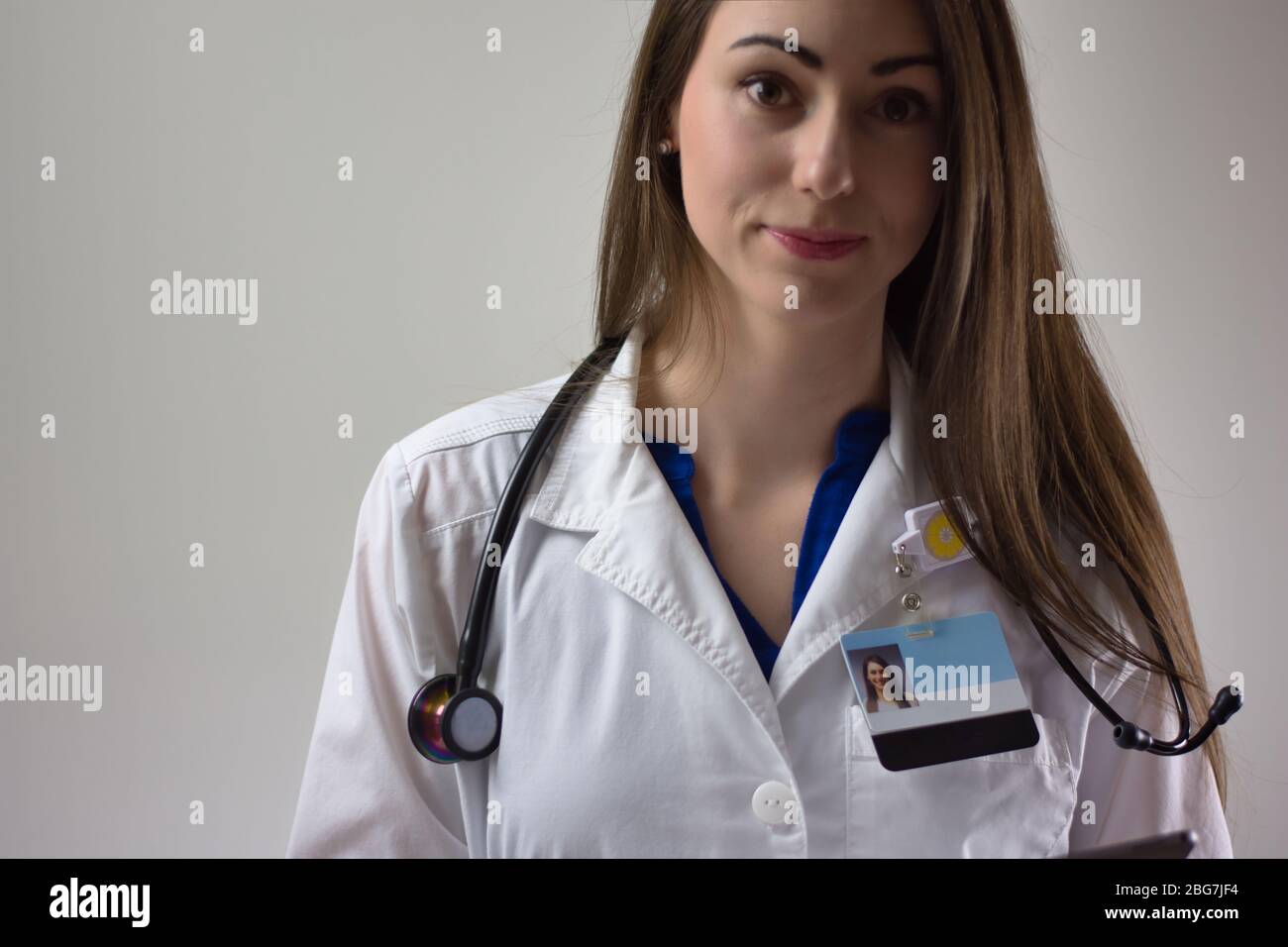 Female physician on grey background. White coat, stethoscope, badge