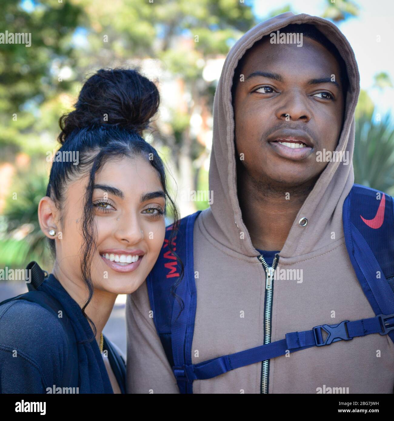 A lovely young woman and man of color, enjoy campus life as students with hoodie and trendy up-do hairstyle and smiles at the U of A in Tucson, AZ Stock Photo