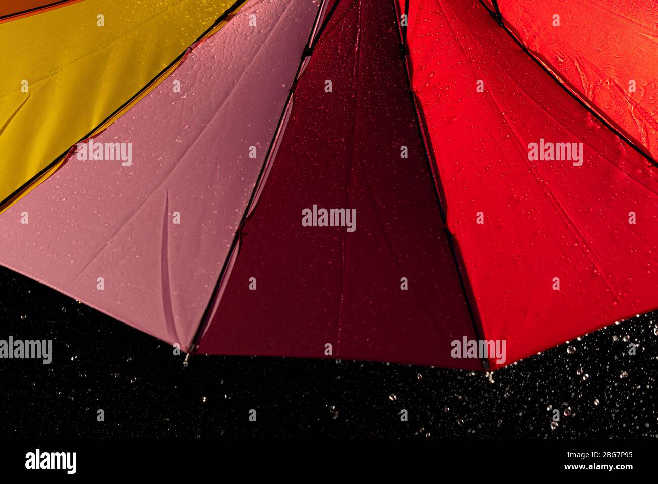 A multi colored rainbow umbrella with rain running down its sides Stock Photo