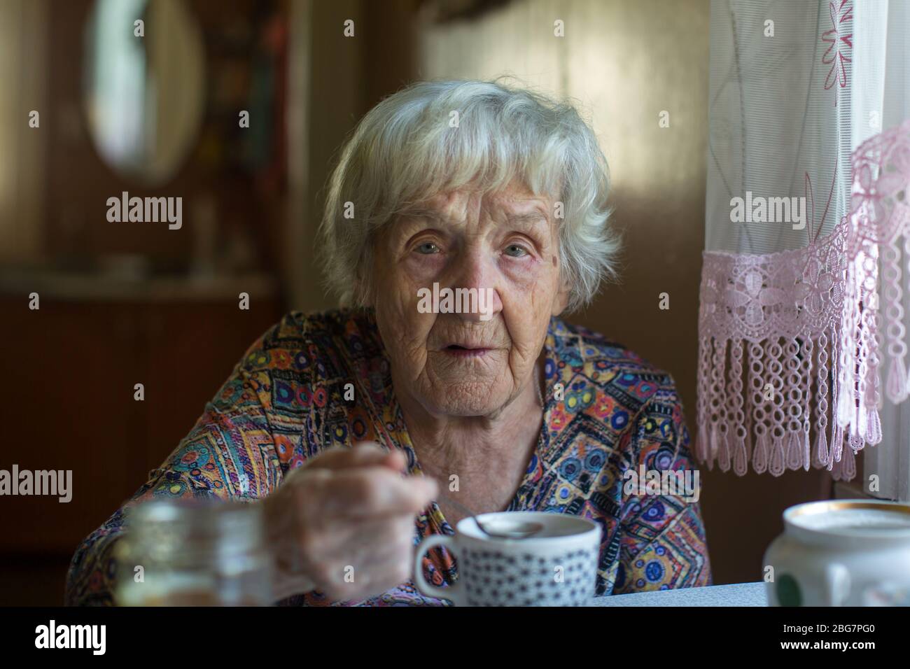 Portrait of an Old woman sitting in the her kitchen. Stock Photo