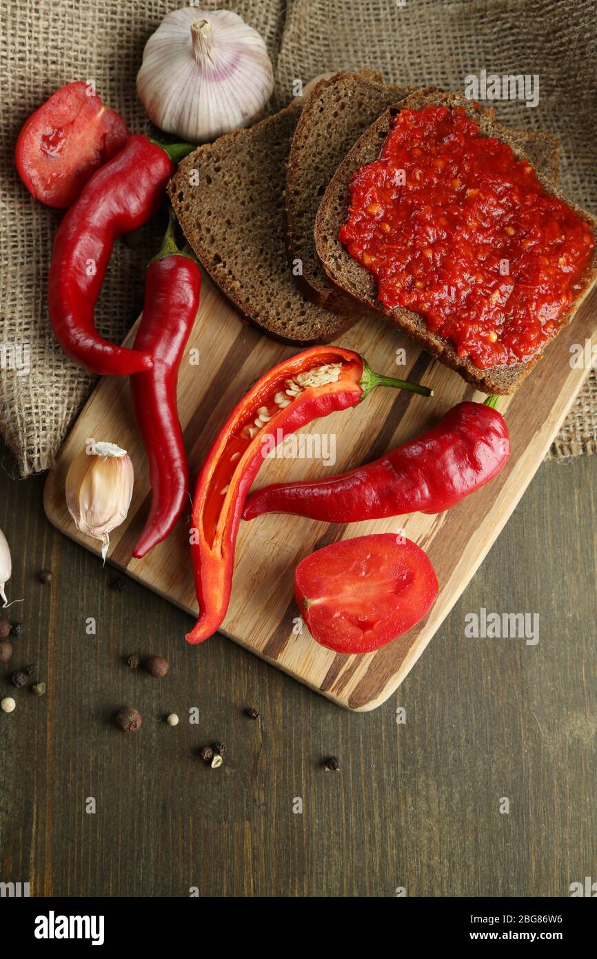 Composition with salsa sauce on bread,, red hot chili peppers  and garlic, on sackcloth,  on wooden background Stock Photo