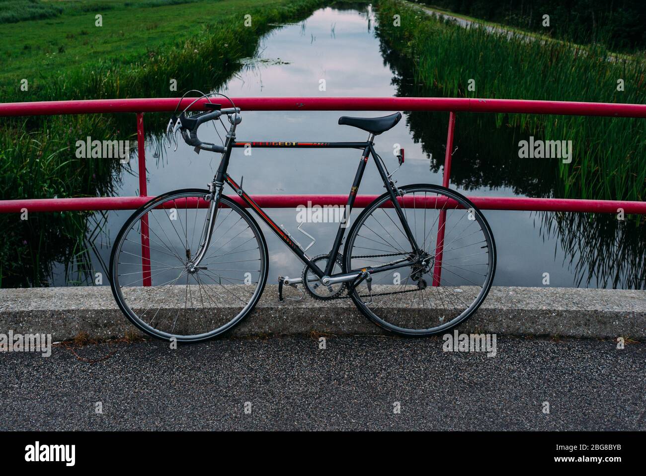 vintage peugeot racing bike leaning on a pink bridge. green lined canal, in background Stock Photo