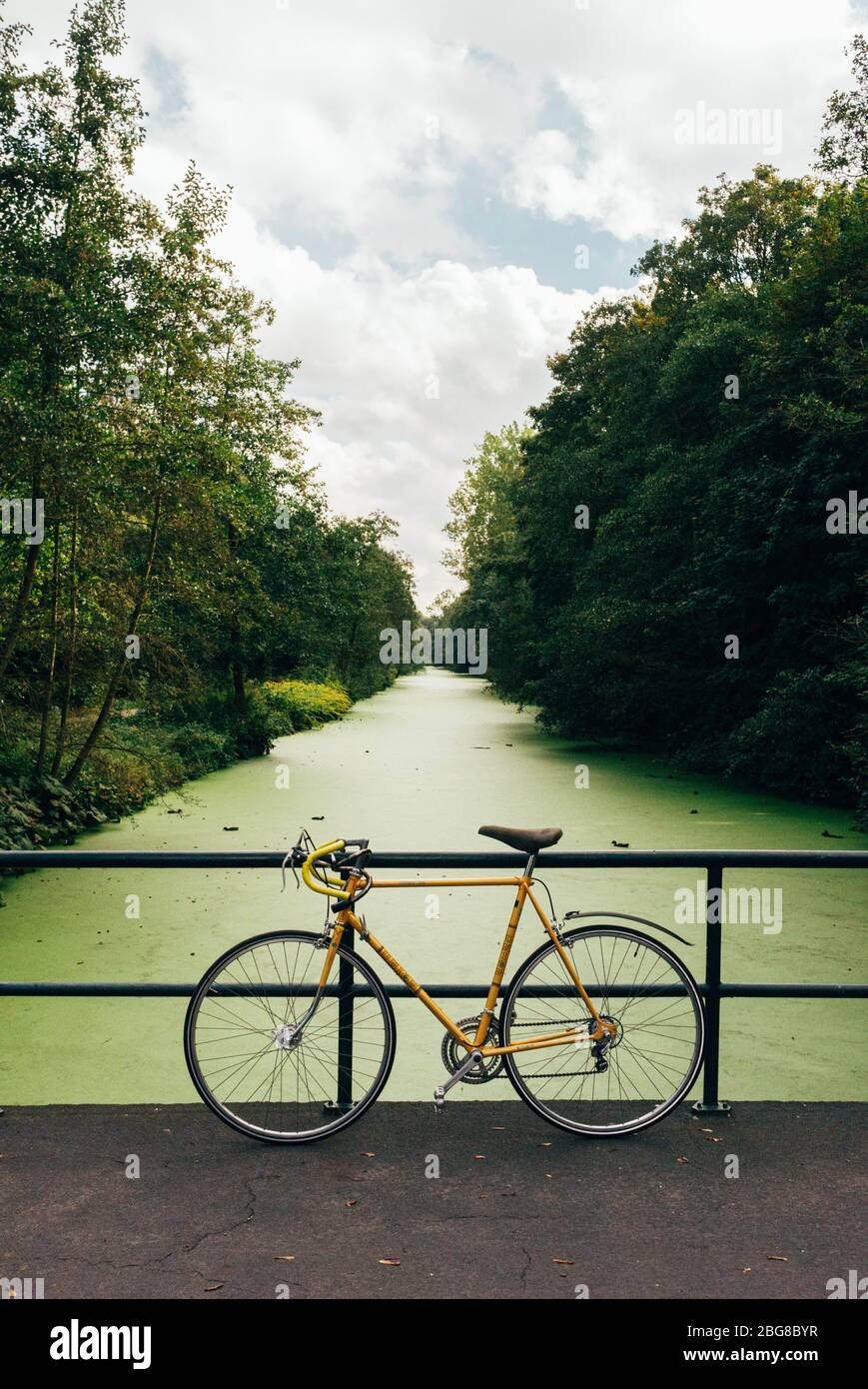 vintage yellow racing bike leaning on a bridge. green lined canal, trees, calm and peaceful background Stock Photo