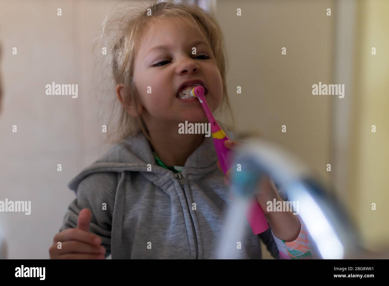Emotional close up of a cute little girl brushing teeth with electric toothbrush Stock Photo