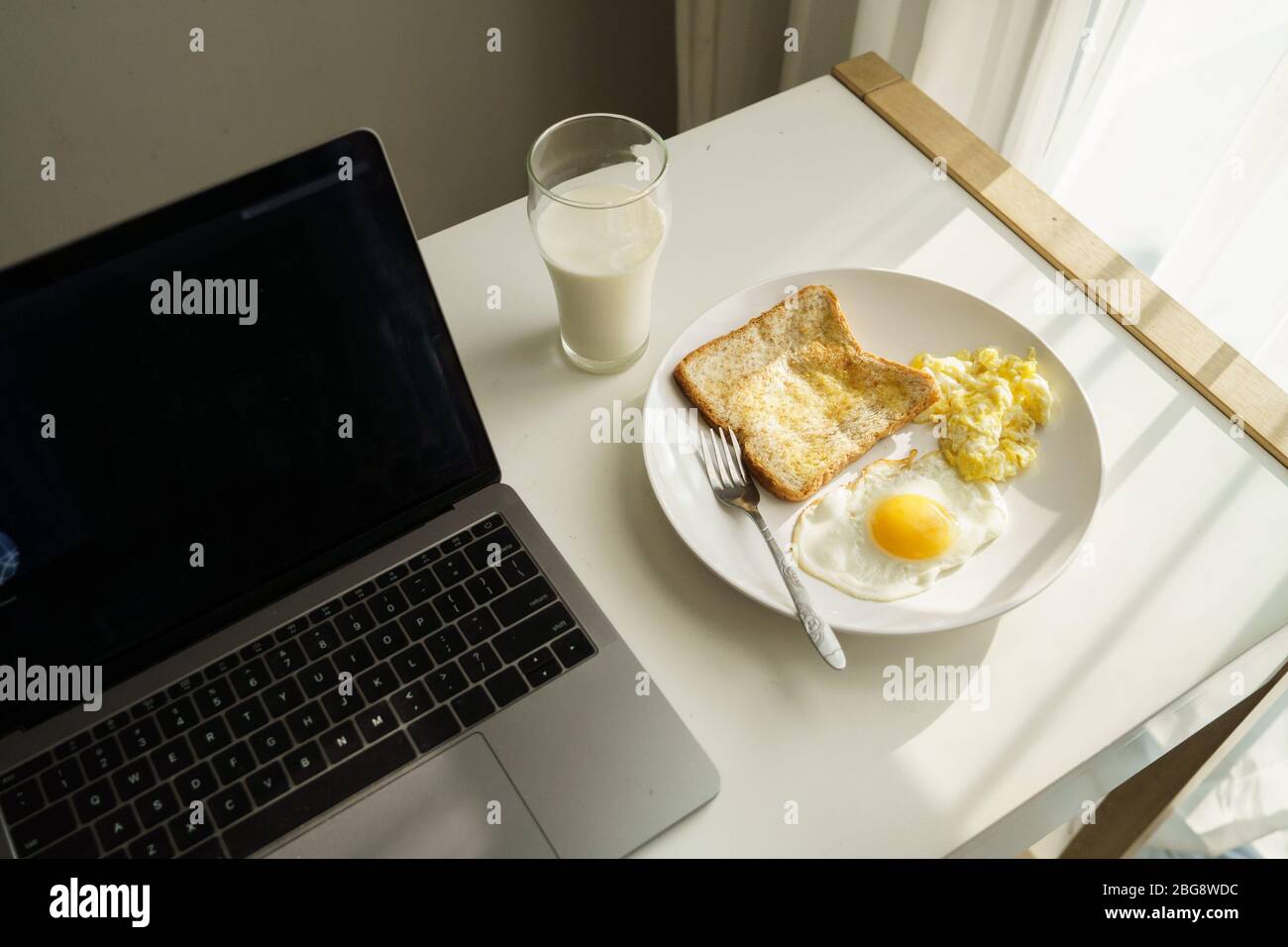 laptop computer on desk with breakfast food of egg and bread toast next ...
